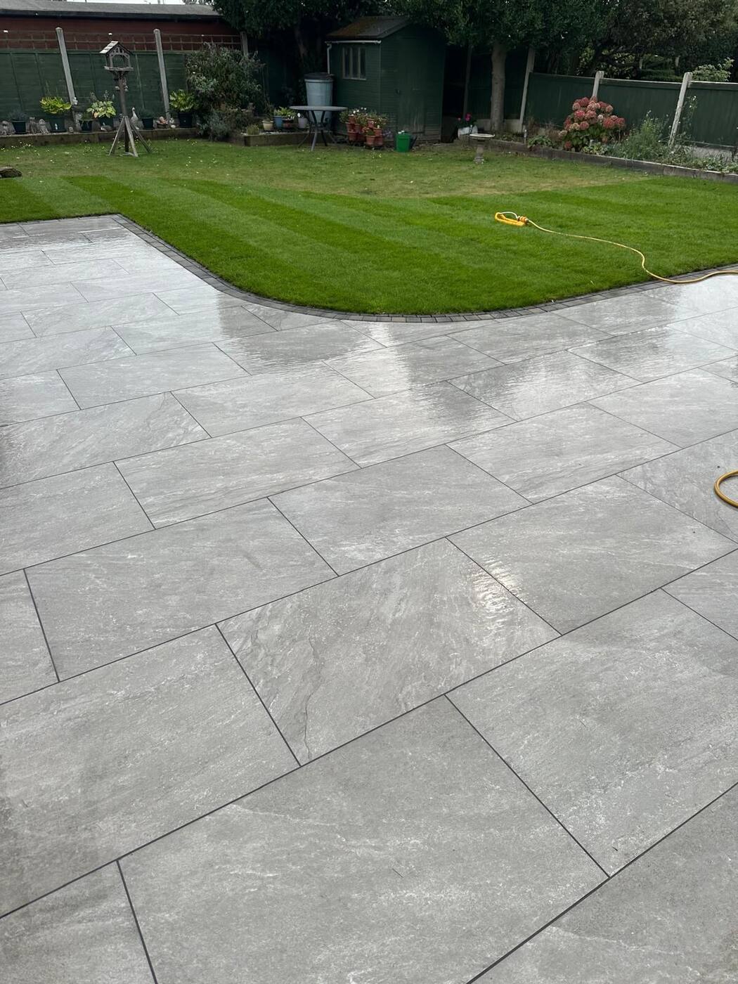 Wet porcelain patio reflecting garden fence, freshly laid